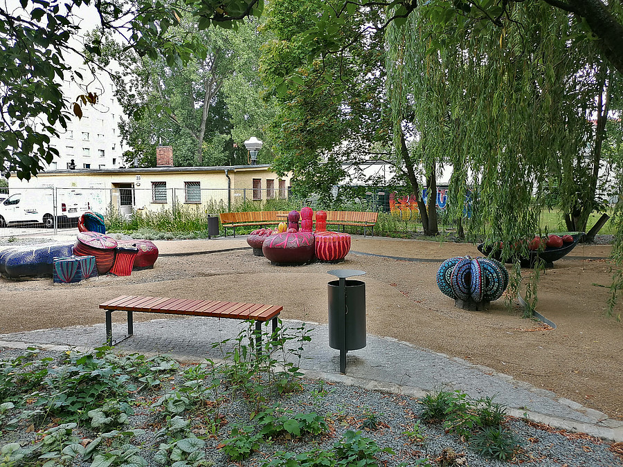 Sitzplatz mit farbigen Skulpturen aus Mosaiksteinen in organischen Formen unter Trauerweide