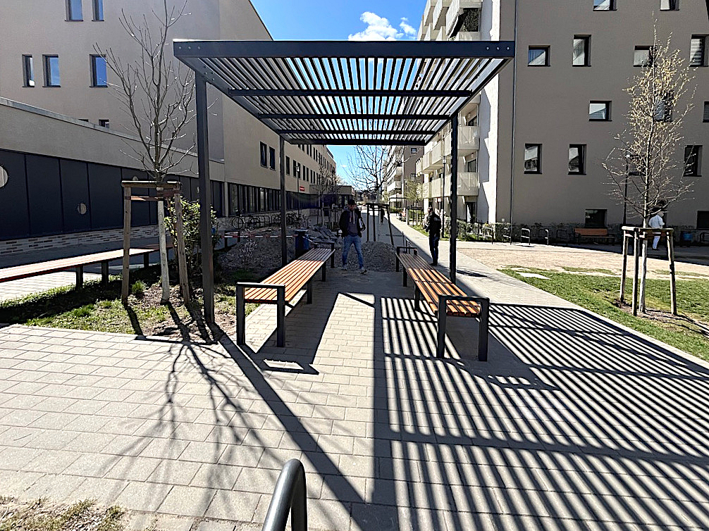 Pergola aus Stahl zwischen Neubauten, jungen Bäume
