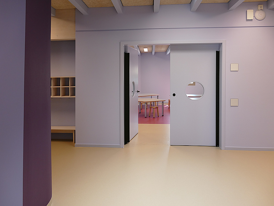 Hell und dunkel violett gefärbter Flur mit Garderobe und offener Tür mit Guckloch
