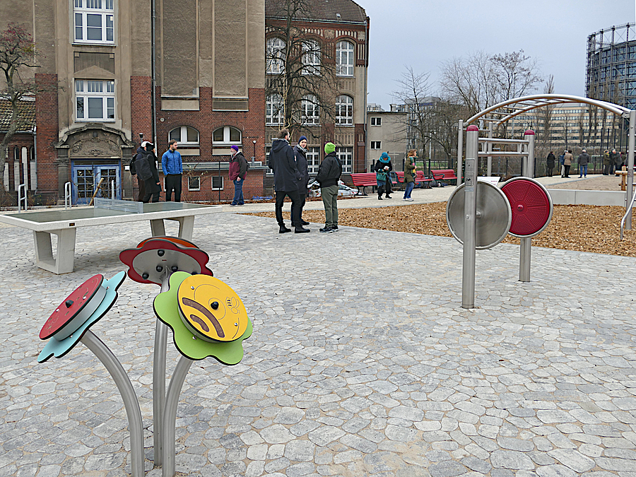 Fläche mit Tischtennisplatte; Blumen-Spiel und Rollstuhltrainer, Im Hintergrund Gasometer