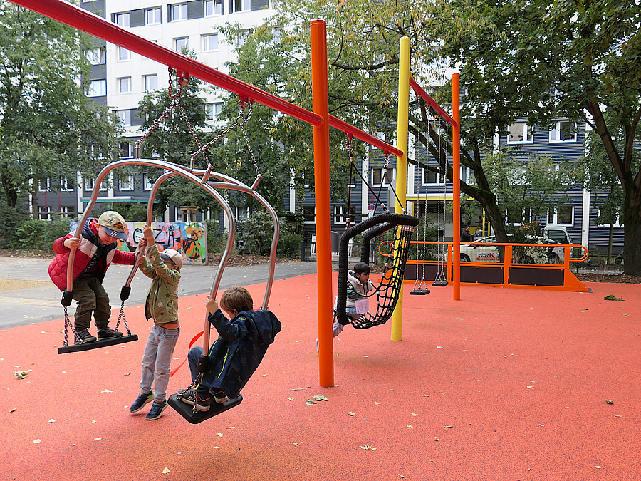 4 Kinder schaukeln auf Schaukelwippe und Sitznestschaukel auf rotem Boden