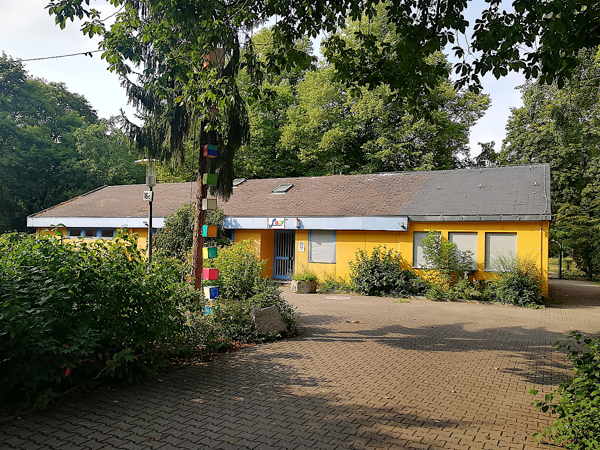 Gelber Flachbau mit Satteldach, Pflaster und Grünfläche