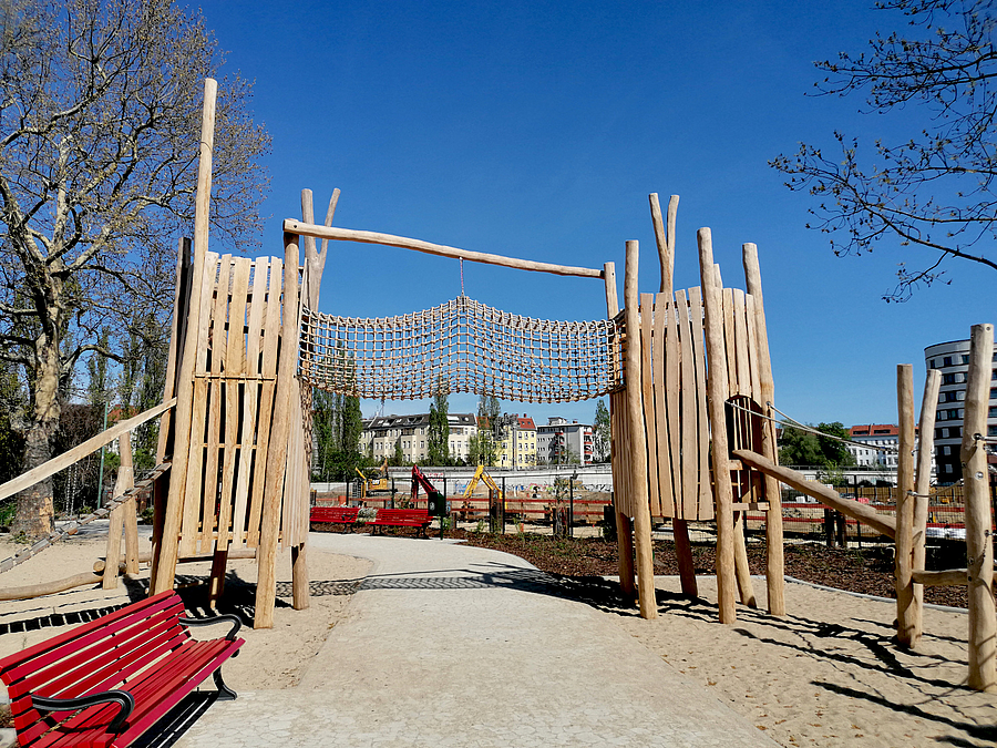 Spielplatz mit Kletterbrücke über den Weg und roter Bank