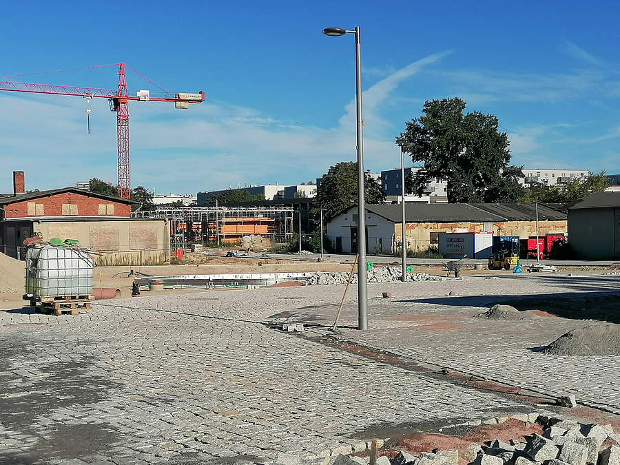 Die Baustelle Anfang September 2023 Baustelle mit großem Pflaster und neuen Mastleuchten, Wirtschaftsgebäude, Grün