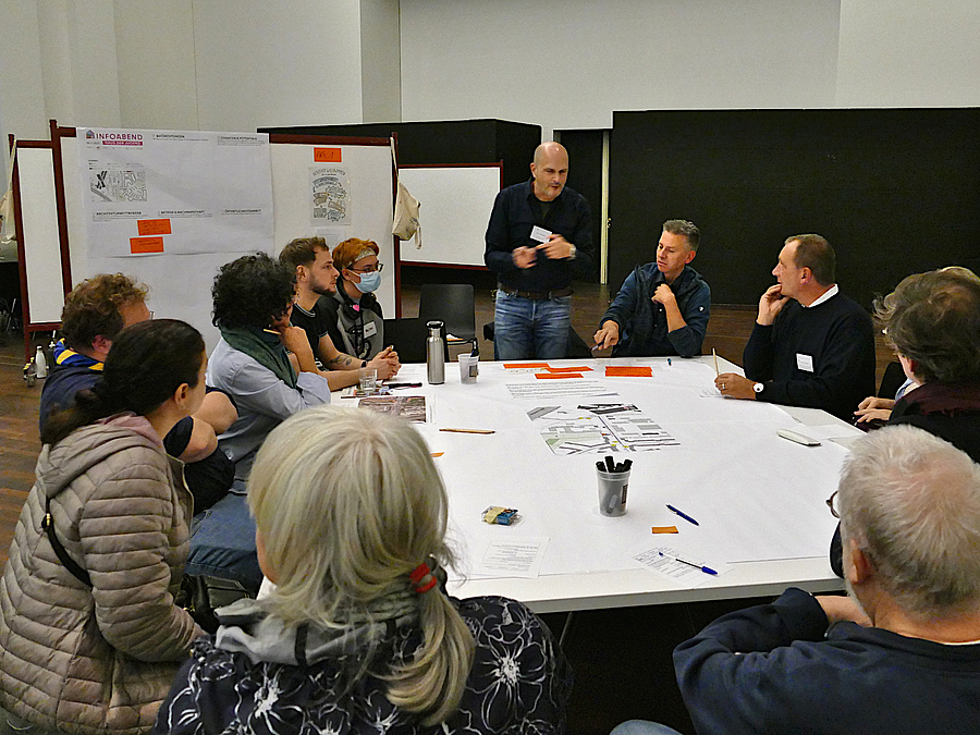Menschen sitzen und stehen um einen Tisch mit Dokumenten und Stiften