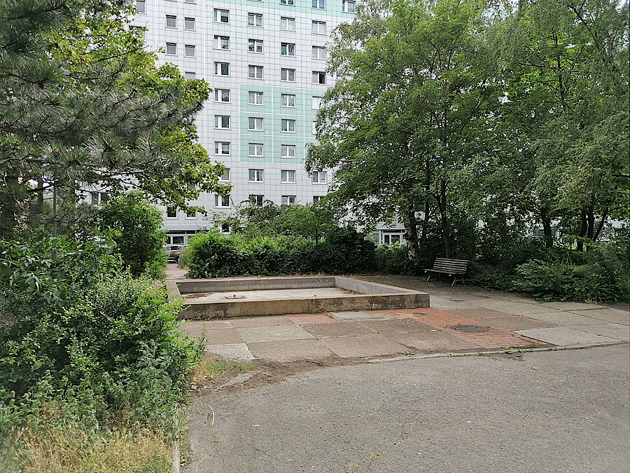 Versiegelter Platz, dahinter Hochhaus, Bäume, Brunnenbecken