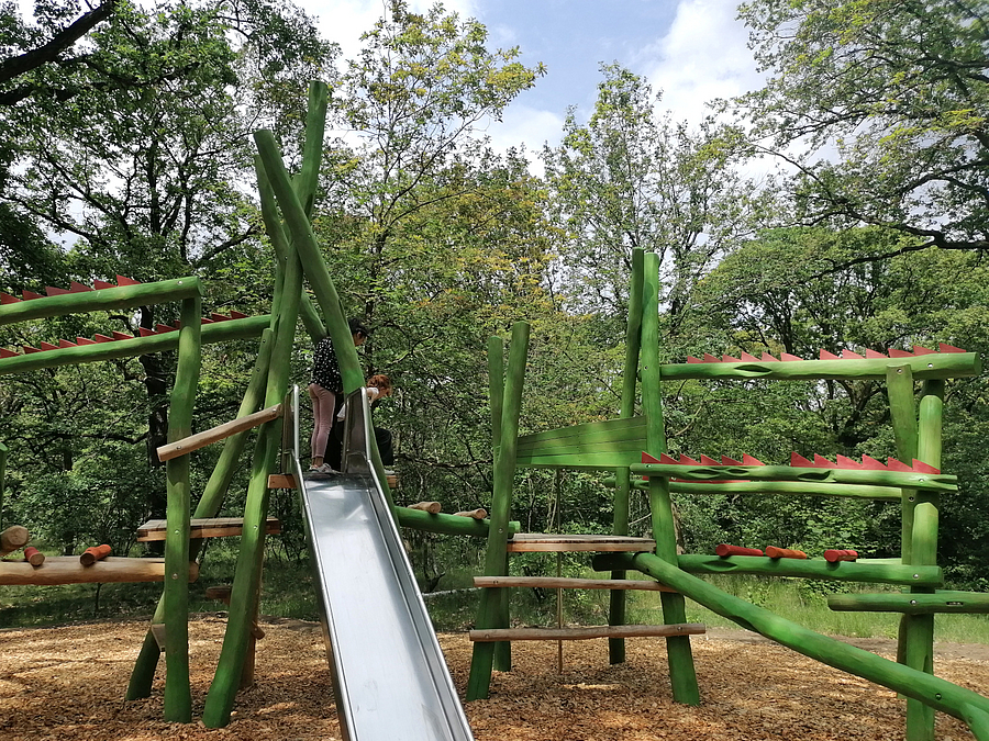 Rutsche an grünem Kletterparcours auf Waldspielplatz