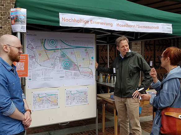 Standbetreuer und Interessierte an großer Karte unter Pavillon