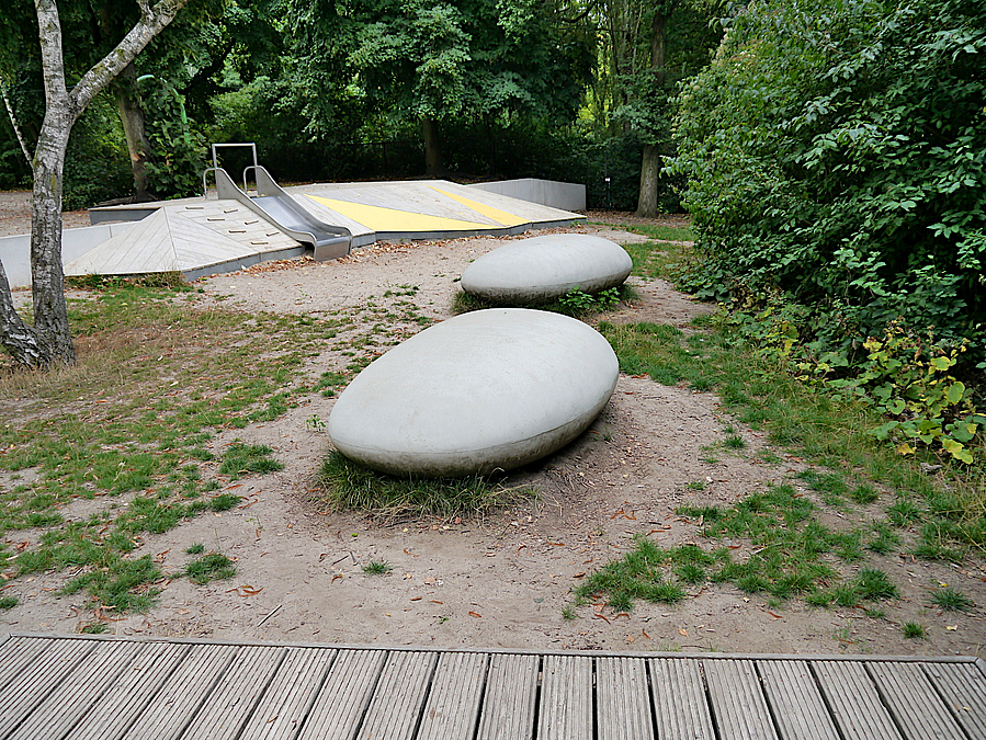 Runde Sitzsteine, dahinter kleine Rutsche auf Holzdeck in grau und gelb