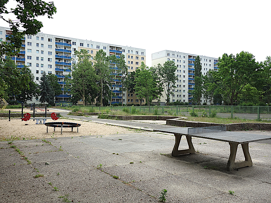 Noch intakte Spielgeräte sollen im Bezirk wieder verwendet werden Plattenbauten, Spielplatz mit Unkraut, Tischtennisplatte, kleinem Sandspielplatz