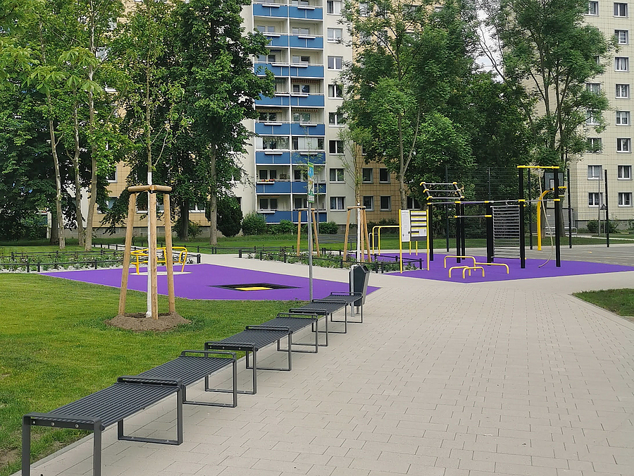 Grün, Weg mit Bänken zu Calisthenics-Anlage auf violettem Boden