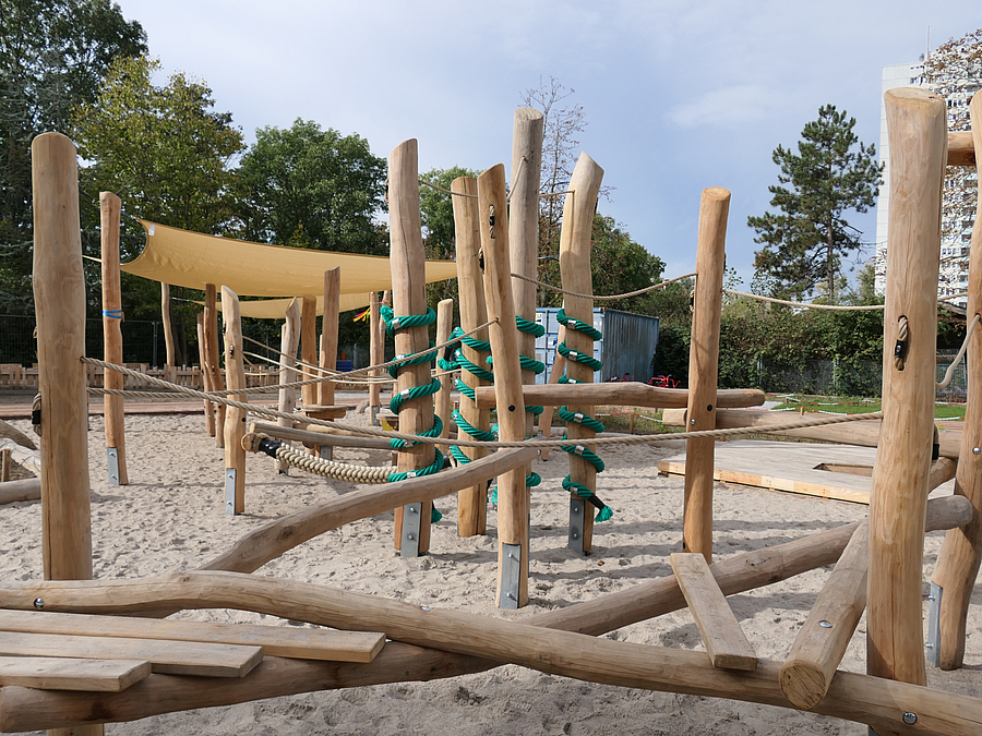 Sandflaeche mit Balancierstrecke und Rutschenturm aus Holz und Seilen mit Sonnensegel