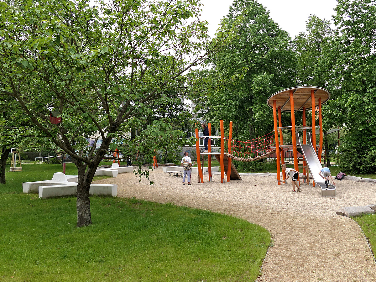 2 Klettertürme mit Rutsche und Seilen als Verbindung in Orange in Garten mit Obstbäumen und weiße Sitzelementen