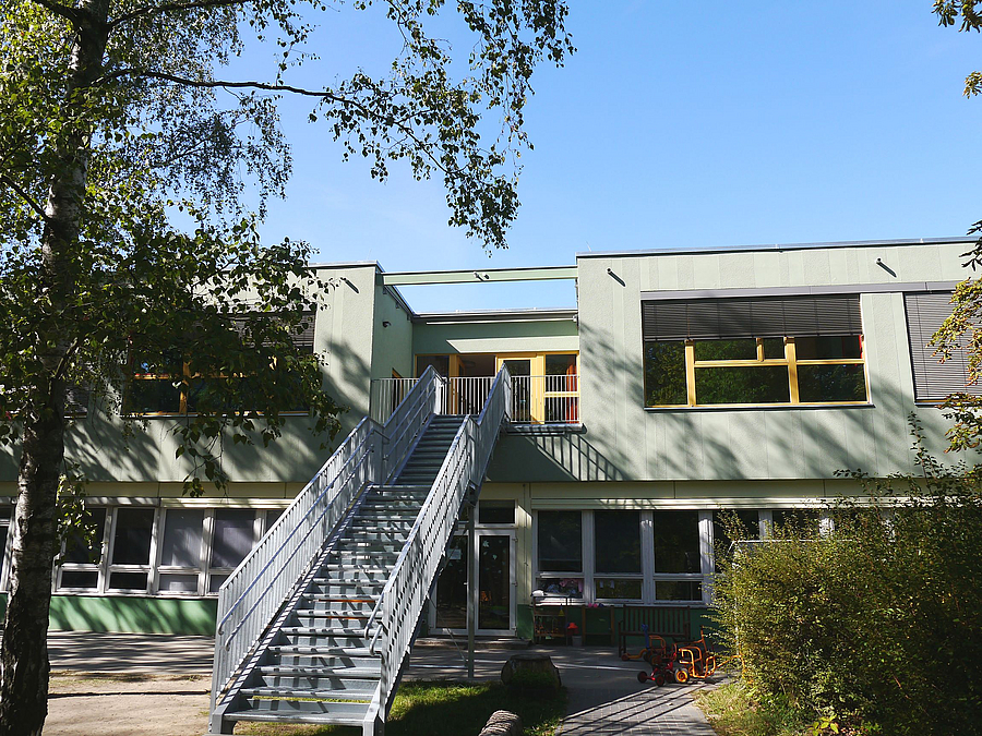 zweistöckige Gebäude in grün hinter Bäumen, Metalltreppe aus dem OG in den Garten