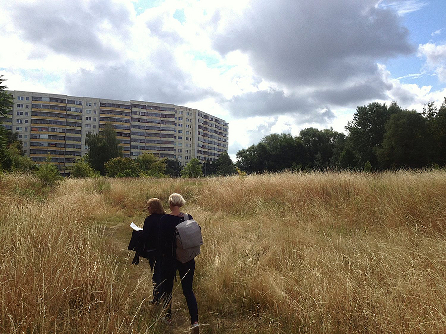 2 Frauen auf Feld, im Hintergrund Plattenbauten und Wald