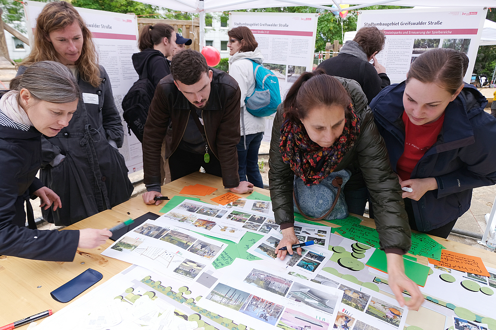 Menschen beugen sich über Papiere mit Fotos und Symbolen