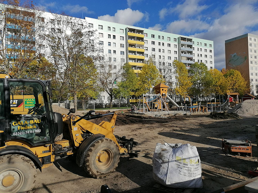 Bagger, Baustelle vor Plattenbau und herbstlichen Bäumen