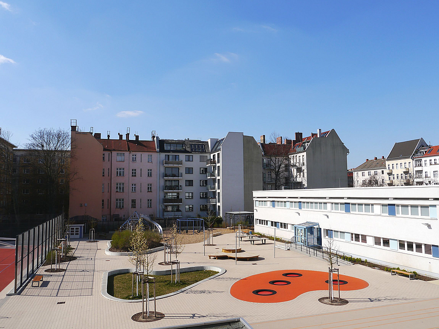 Gepflasterter Hof mit organisch geformten Feldern in orange mit Trampolinen und grün mit Bäumen