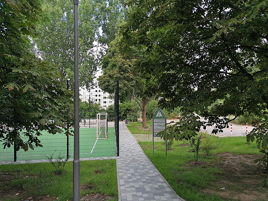 Blick on oben auf Bolzplatz, Grünanlagen-Schild, neu gepflanzten Baum und Fahrradbügel