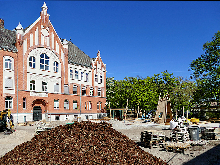 Baustelle mit altem Schulgebäude und Holzhäckselhaufen für Beete