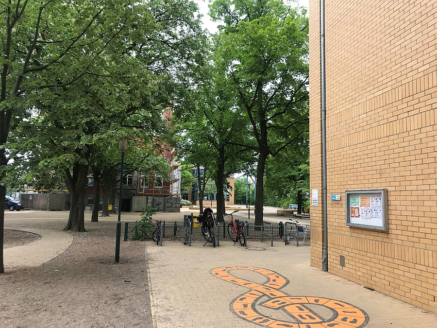 Gebäudeecke mit Plattenweg und Hüpfspiel, Schulhof mit Bäumen