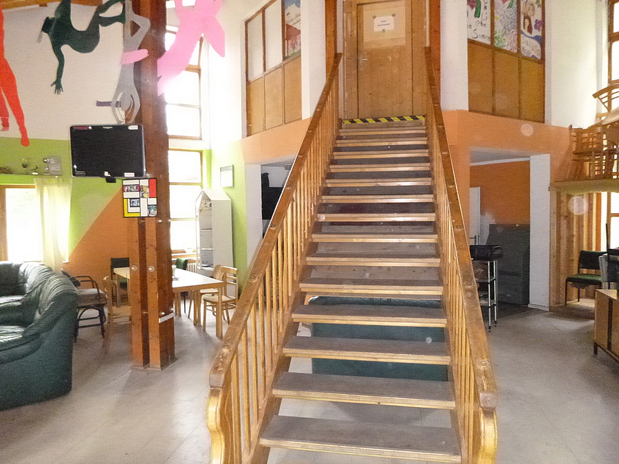 Hoher Innenraum mit Holztreppe zu abgeteiltem Bereich