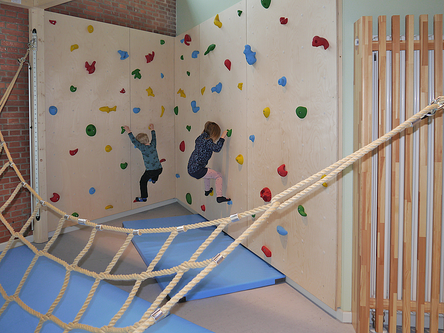 2 Kinder an Boulderwand in Ecke, davor Kletterhängematte