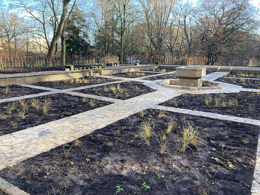 Gitter aus frisch bepflanzten Beeten und Wegen aus Kalsteinplatten. Brunnen im Zentrum