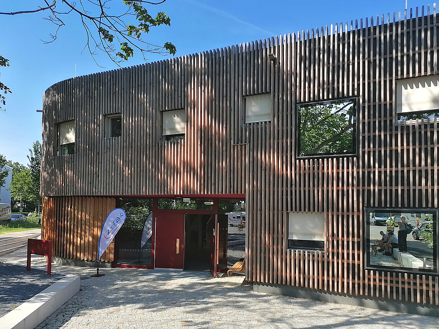 Holzlatten-Fassade eines zweistöckigen Gebäudes mit asymmetrischen Fenstern und Eingang