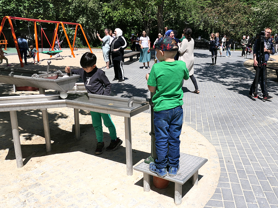 2 Kinder spielen an Pumpe und Wasserrinne auf Spielplatz
