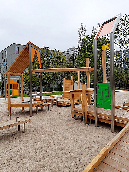 Das meiste ist über breite Stege gut im Rollstuhl erreichbar Holzsteg über Sandspielfläche, Tafel mit Geschicklichkeitsspeil