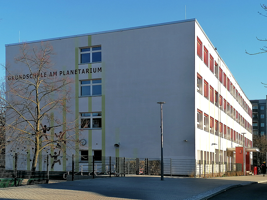 Giebel einer Plattenbauschule mit Schriftzug und stilisierten Sportlern