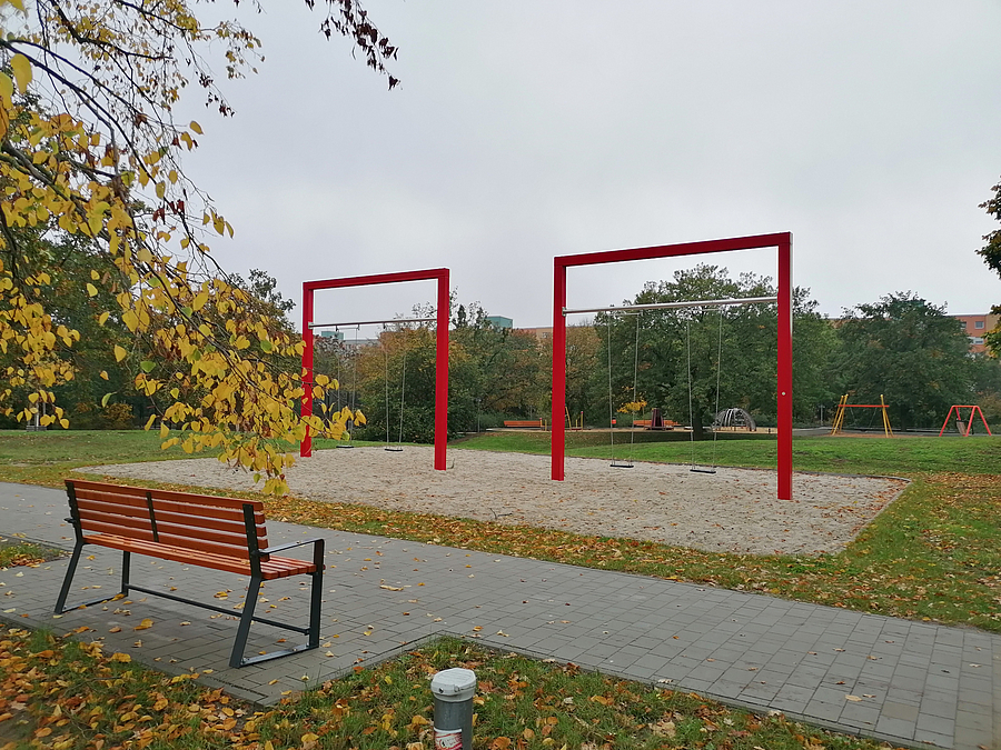 Rote Riesenschaukeln auf Sand im herbstlichen Park und Sitzbank