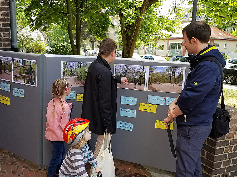 2 Männer und 2 Kinder an Stellwand mit Fotos und Notizen