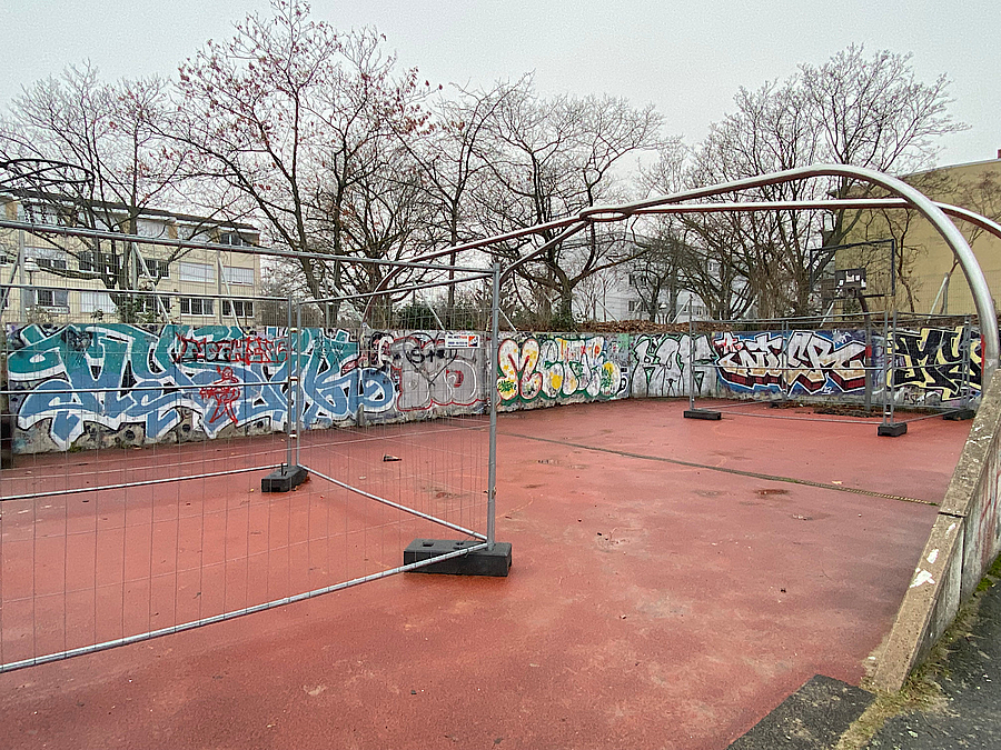Mauer mit Graffiti auf rotem Kunststoffboden mit Bauzäunen
