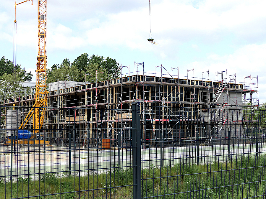 Blick durch Zaun auf eingerüsteten Rohbau und Kran