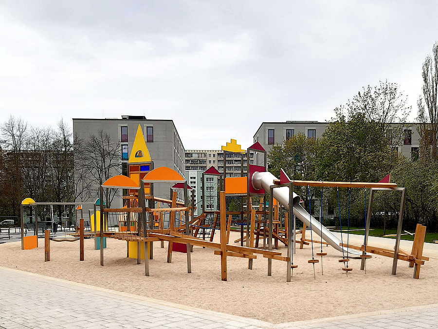 Spielplatz "Dorf der Zukunft" vor Großstadtkulisse Spielplatz mit Rutsche und Kletterparcours, dahinter MUF und Plattenbauten