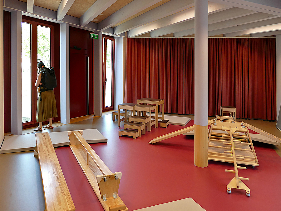 Raum mit Deckenbalken und Säule als Stütze, rote Vorhänge und Boden, Sportgeräte für Kleinkinder aus Holz