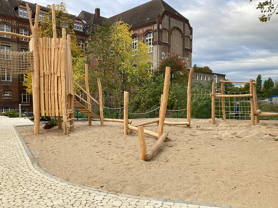 Sandspielfläche mit Holzturm, altes Schulgebäude im Hintergrund