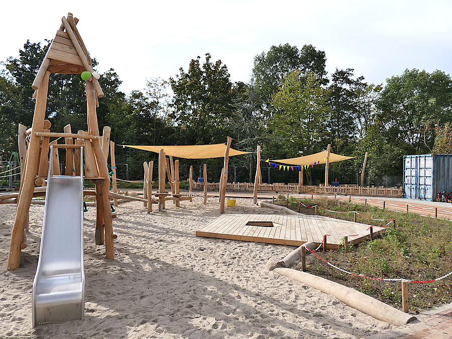 Sandfläche mit Balancierstrecke und Rutschenturm aus Holz und Seilen mit Sonnensegel, Beet