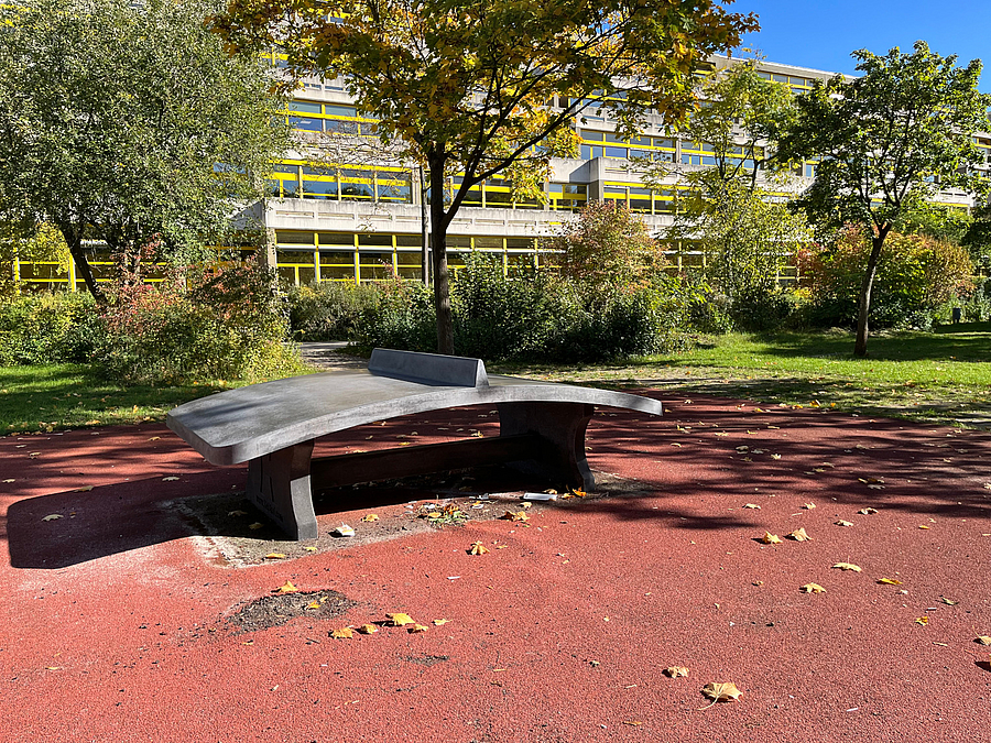 Blick auf den Schulhof des Thomas-Mann-Gymnasiums vor der Neugestaltung Gekrümmte Tischtennisanlage auf beschädigtem Boden, herbstliche Bäume und Laubengang
