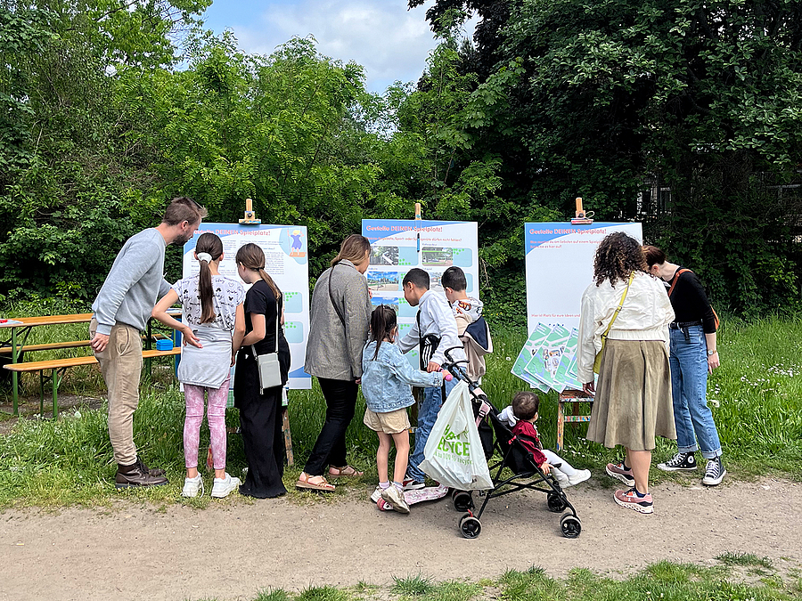 Kinder beteiligen sich am 4. Mai 2024 vor Ort an der Ideenfindung für den Spielplatz Kinder mit Erwachsenen an Pinnwänden im Freien
