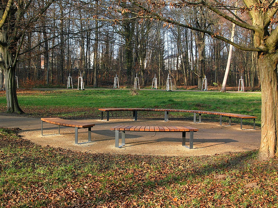 Neue Rundbank im nördlichen holländischen Garten  Zwei halbe Rundbänke aus Holz ohne Lehne an gegenüberliegenden Seiten einer runden Aufweitung eines Weges, Bäume im Frühling