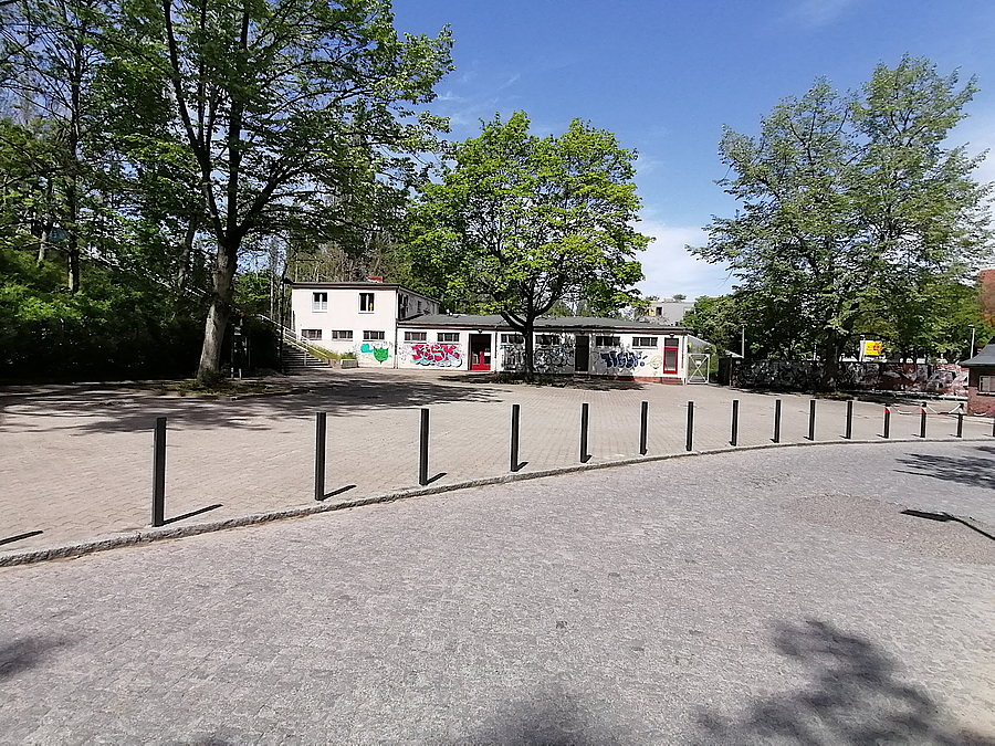 Platz mit Pollern, Bäumen, weißem, niedrigem Gebäude