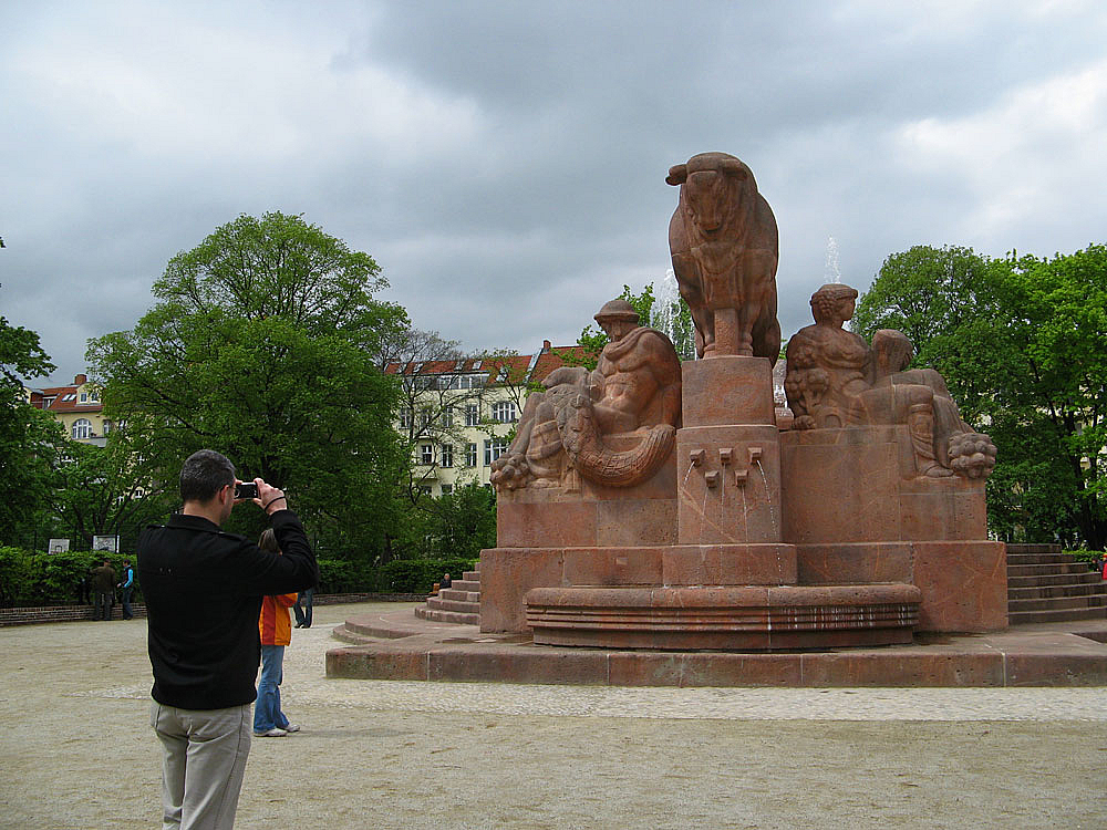 Stierstatue aus rotem Stein auf Platz, Fotograf, Laubbäume