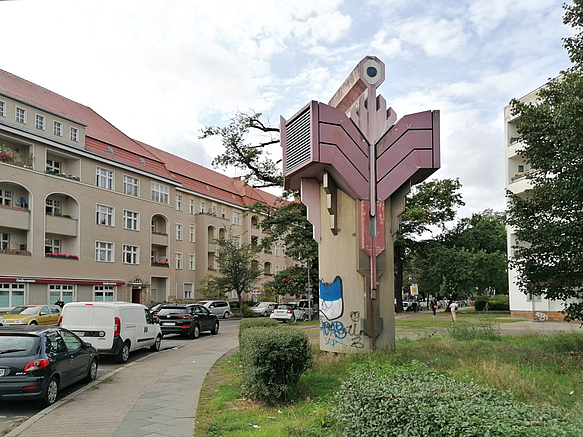 Gebogener Wohn-Riegel mit Loggien, Stein-Skulptur aus geometrischen Formen auf Grünfläche