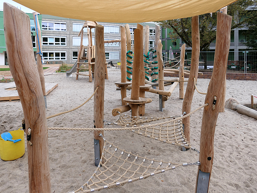 Sandflaeche mit Balancierstrecke und Rutschenturm aus Holz und Seilen mit Sonnensegel