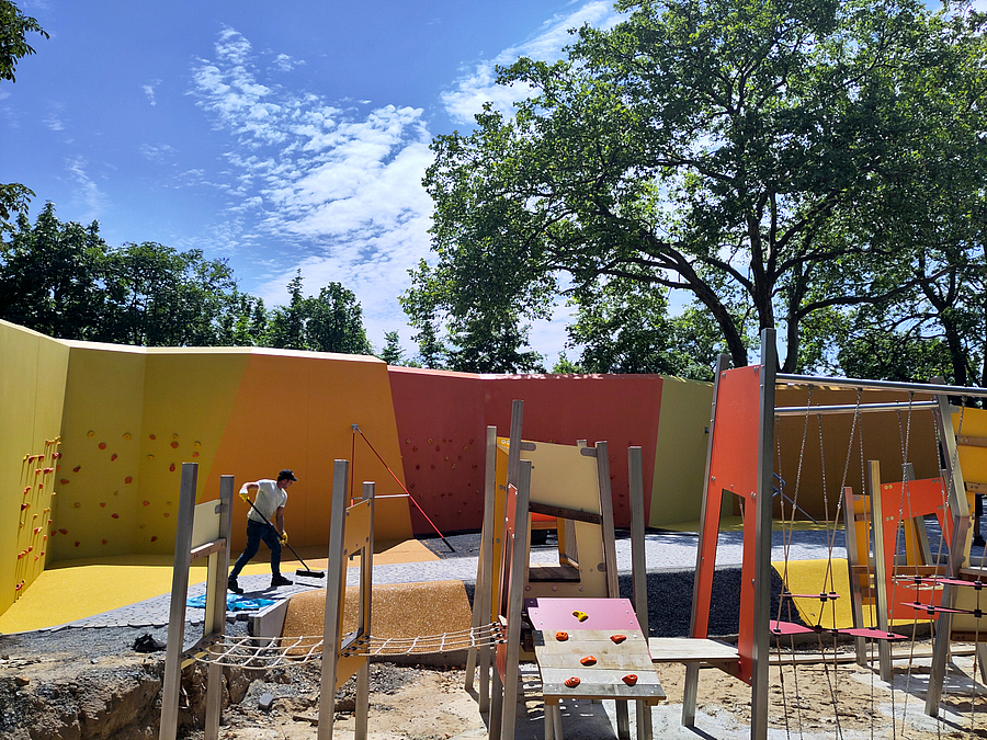 Spielgeräte im Bau, im Hintergrund Wand mit Knicken in Rot, Orange und Gelb