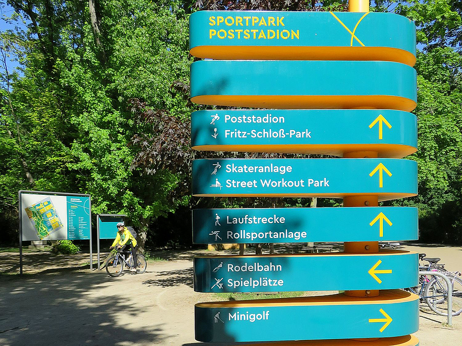Wegweiser-Stele, im Hintergrund großer Lageplan und Radfahrer
