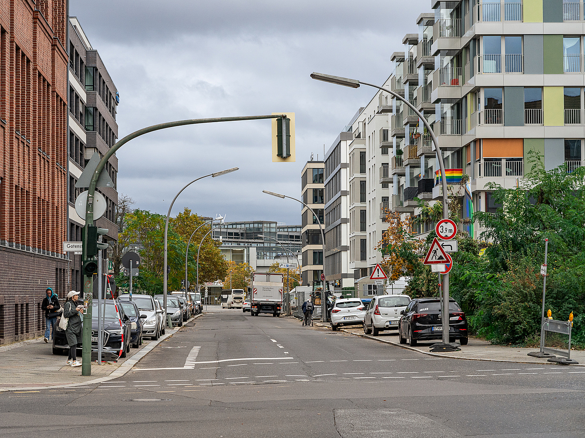 Straße mit Geschäfts- und Wohnbauten und auf dem Gehweg parkenden PKW